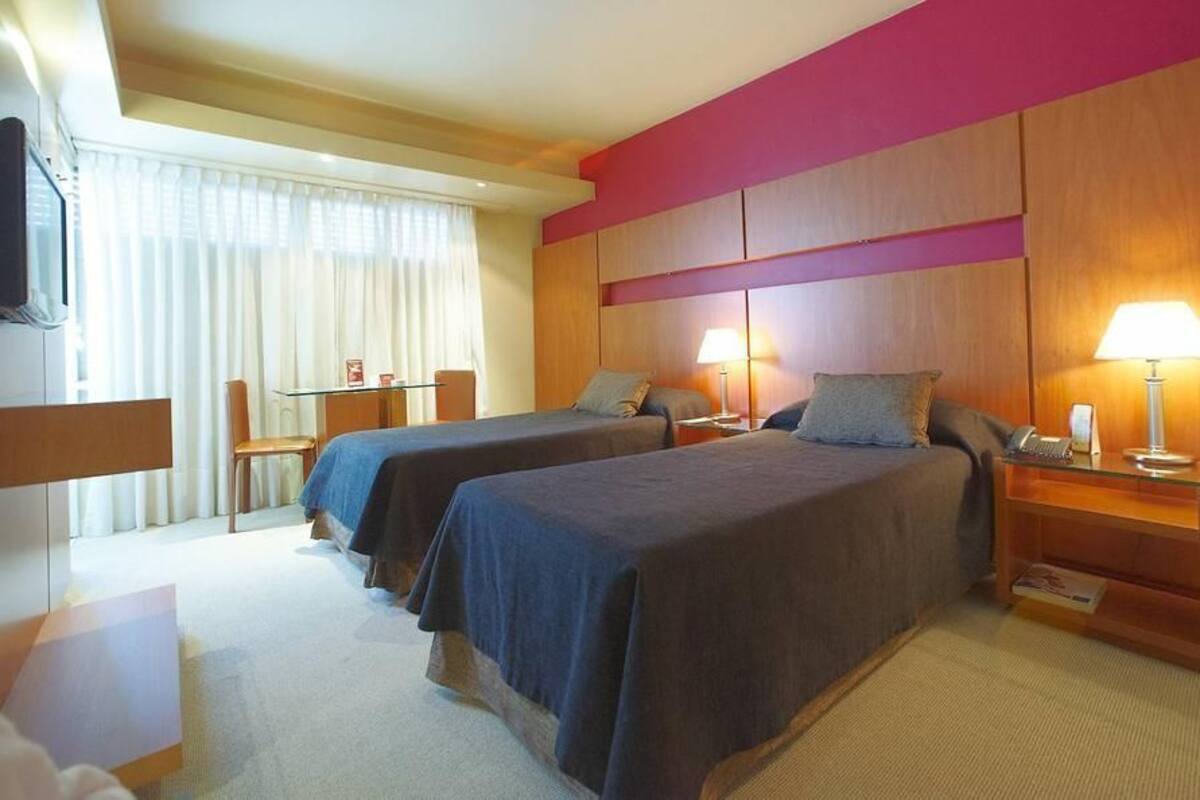 A hotel room with two beds, a desk, a chair, a TV, and a lamp.
