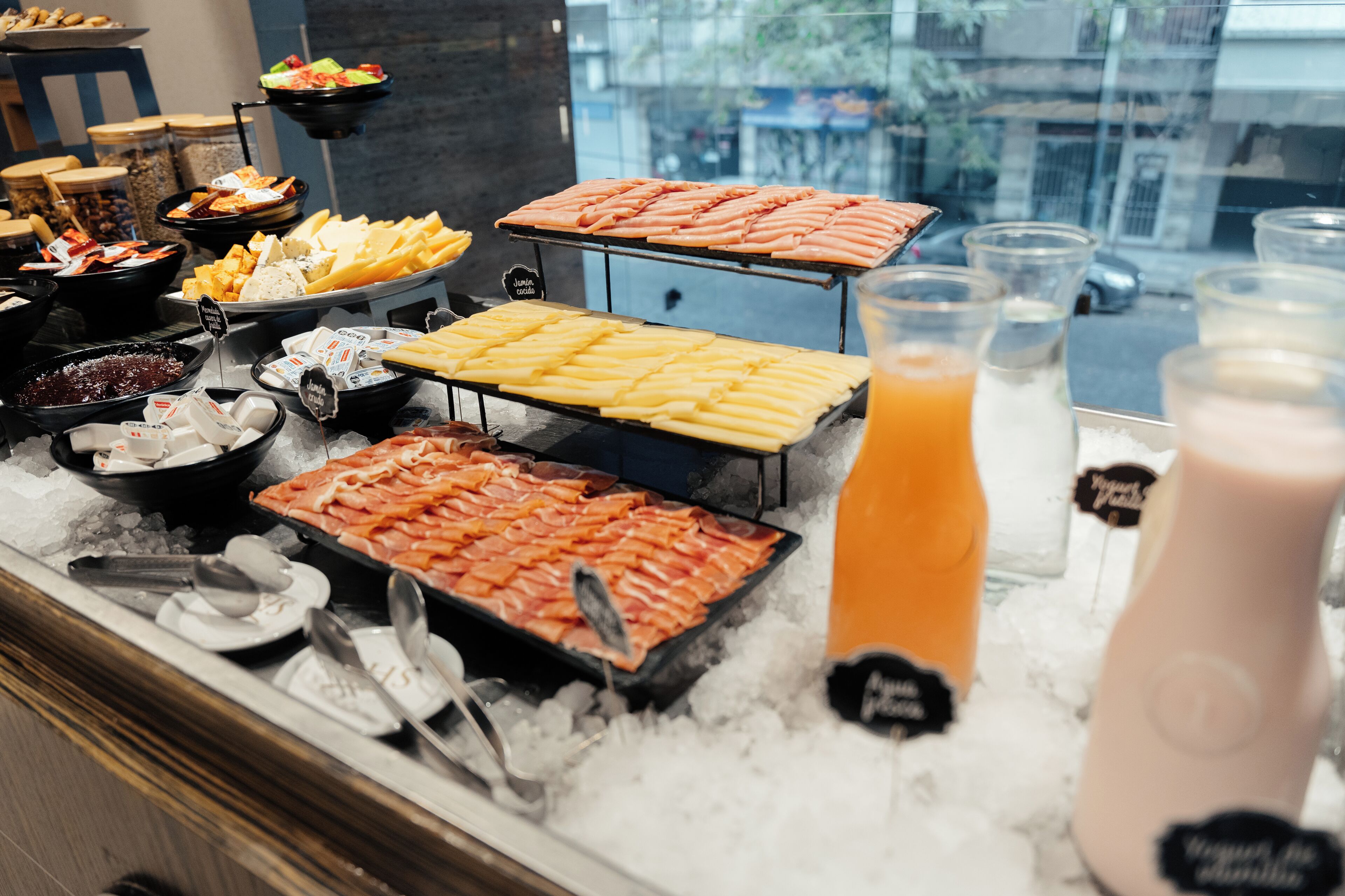 Un bufé con diversas opciones de comida y bebidas, incluyendo carnes, quesos y una ensalada de frutas.