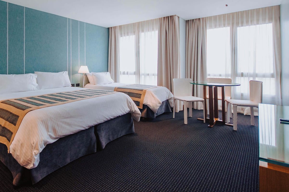 A hotel room with two beds, a glass table, and a chair.