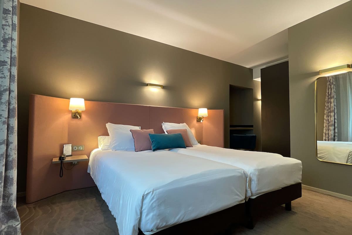 A double bed with white linens, two bedside lamps, and a nightstand with a phone and a sign.