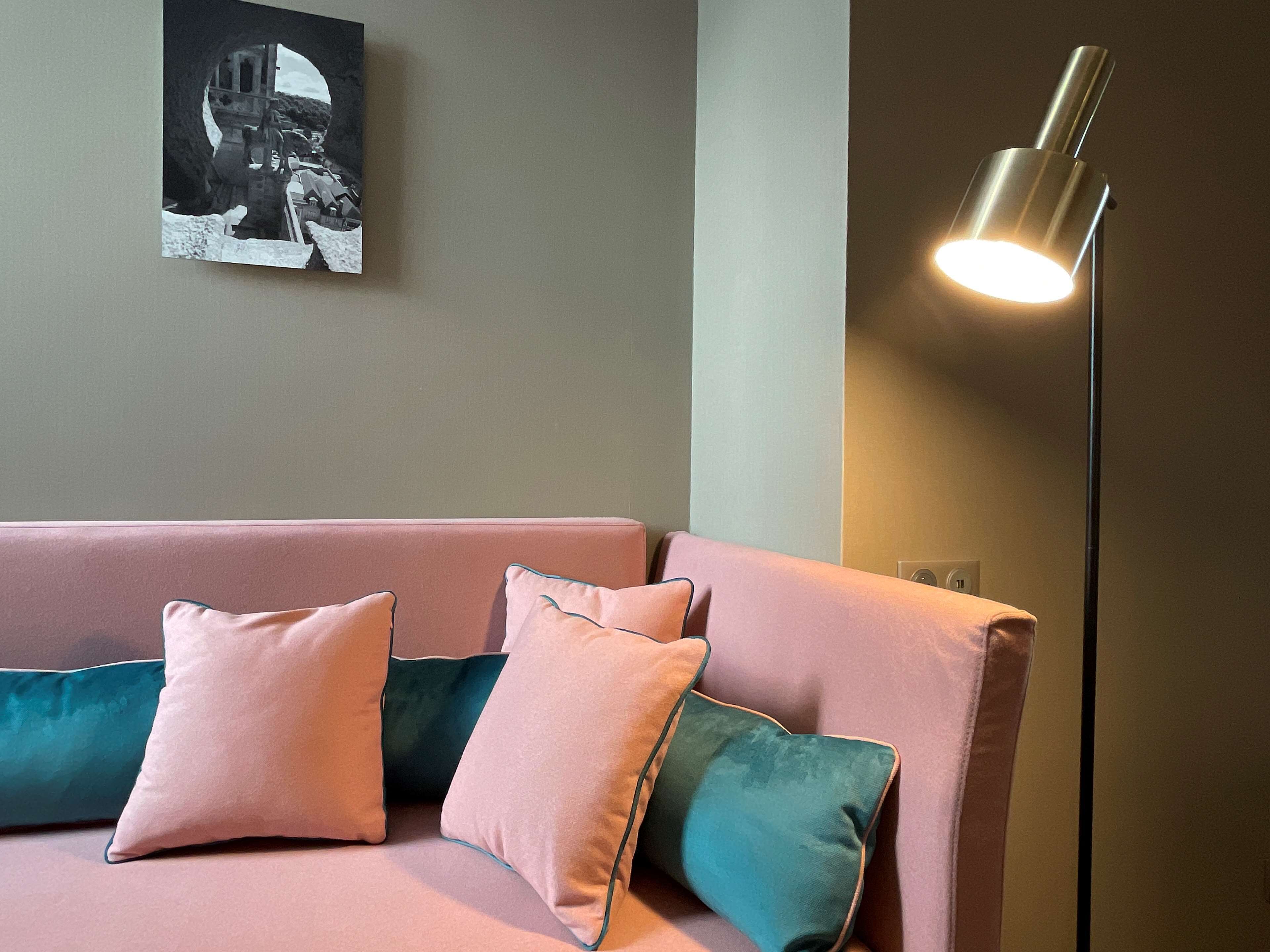 Un salon moderne avec un canapé rose, des coussins turquoise et un lampadaire.