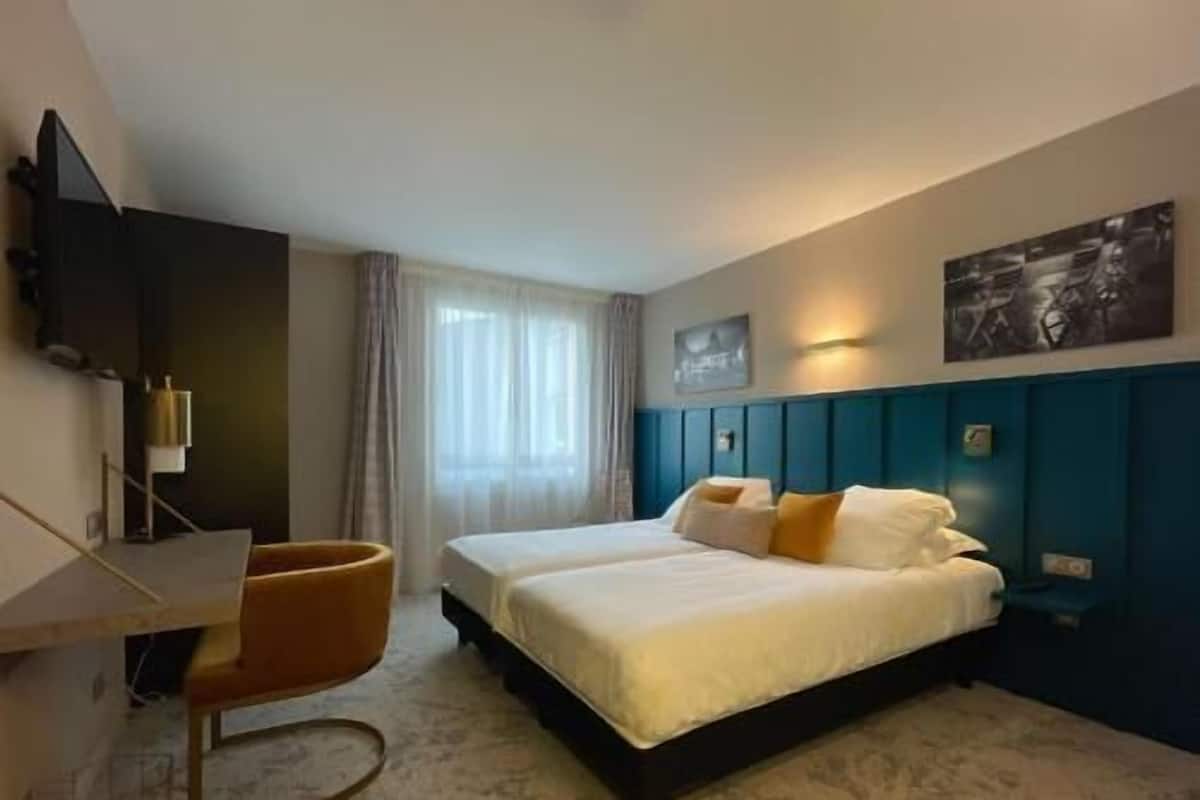 A hotel room with a bed, a desk, a chair, a TV, and a painting on the wall.