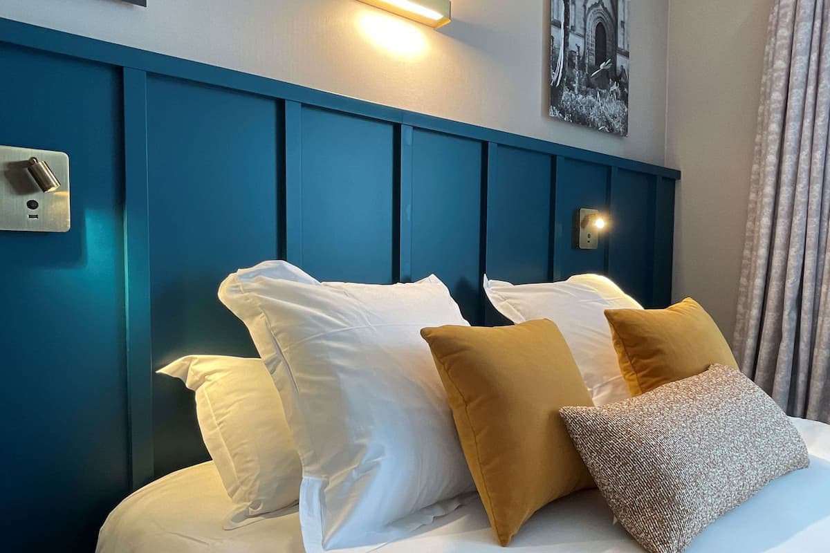 A hotel room with a blue headboard, white bedding, and a painting above the bed.