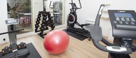 Un gimnasio en casa con equipo de ejercicio, incluyendo una cinta de correr, una elíptica y una pelota de ejercicios roja de gran tamaño.