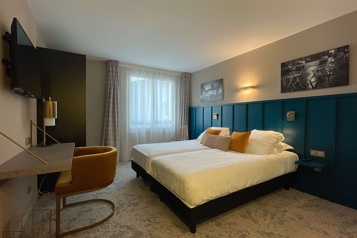 A hotel room with a bed, a desk, a chair, a television, and a window with curtains.