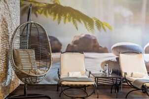 A lounge area with wicker chairs, a hanging chair, and a table with glasses and a bottle.