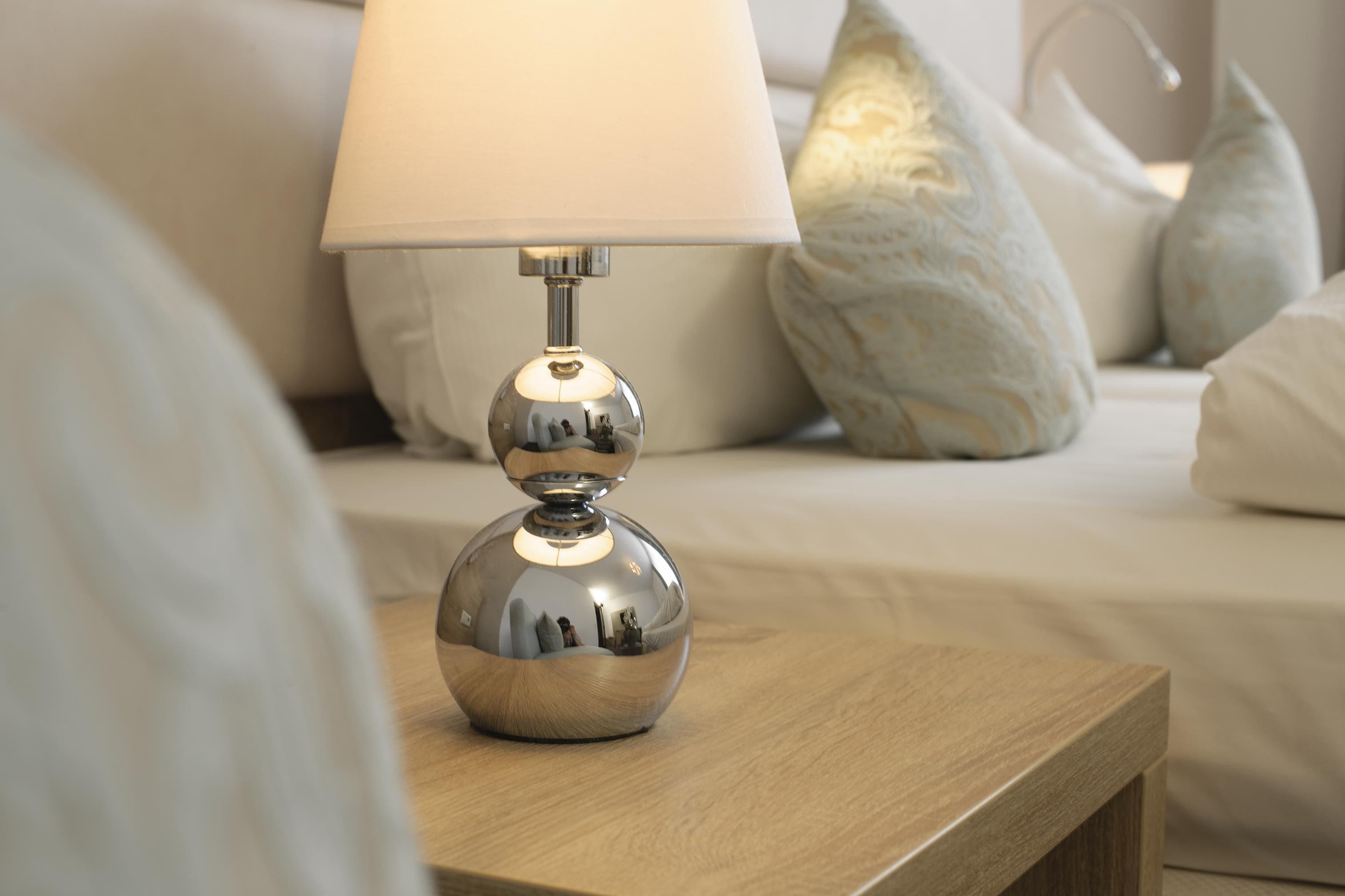 Una lámpara de mesa metálica con una base esférica y una pantalla cónica sobre una mesita de noche de madera.