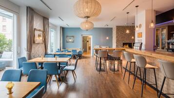Un interior de restaurante moderno con mesas de madera y sillas azules, una zona de bar con taburetes y una pared de piedra.