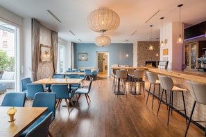 A modern restaurant interior with wooden tables and blue chairs, a bar area with stools, and a stone wall. - Best Western Hotel Lamm (Singen)