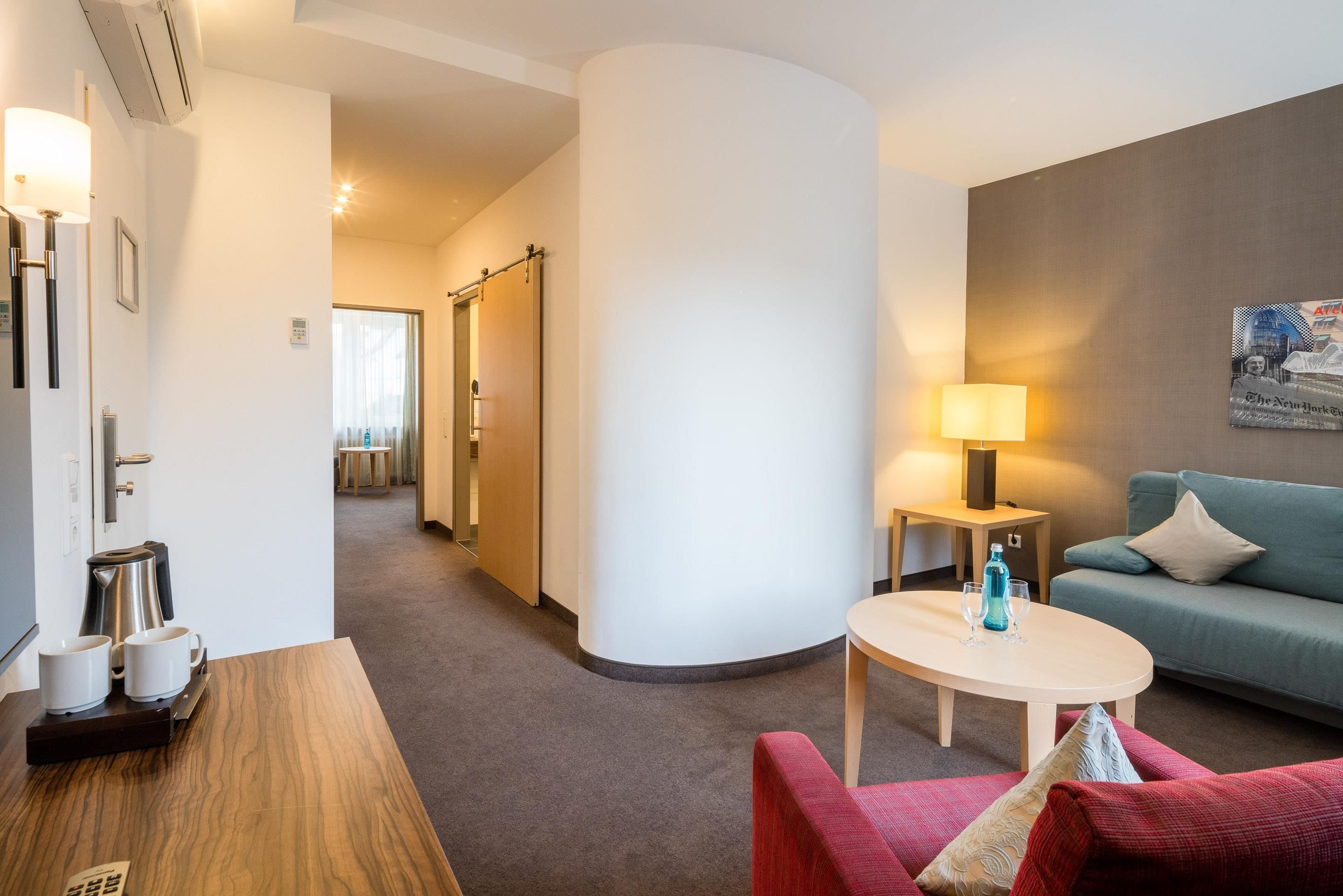 Ein Hotelzimmer mit einer Couch, einem Tisch mit zwei Gläsern und einer Flasche, einer Lampe und einem Bild an der Wand.