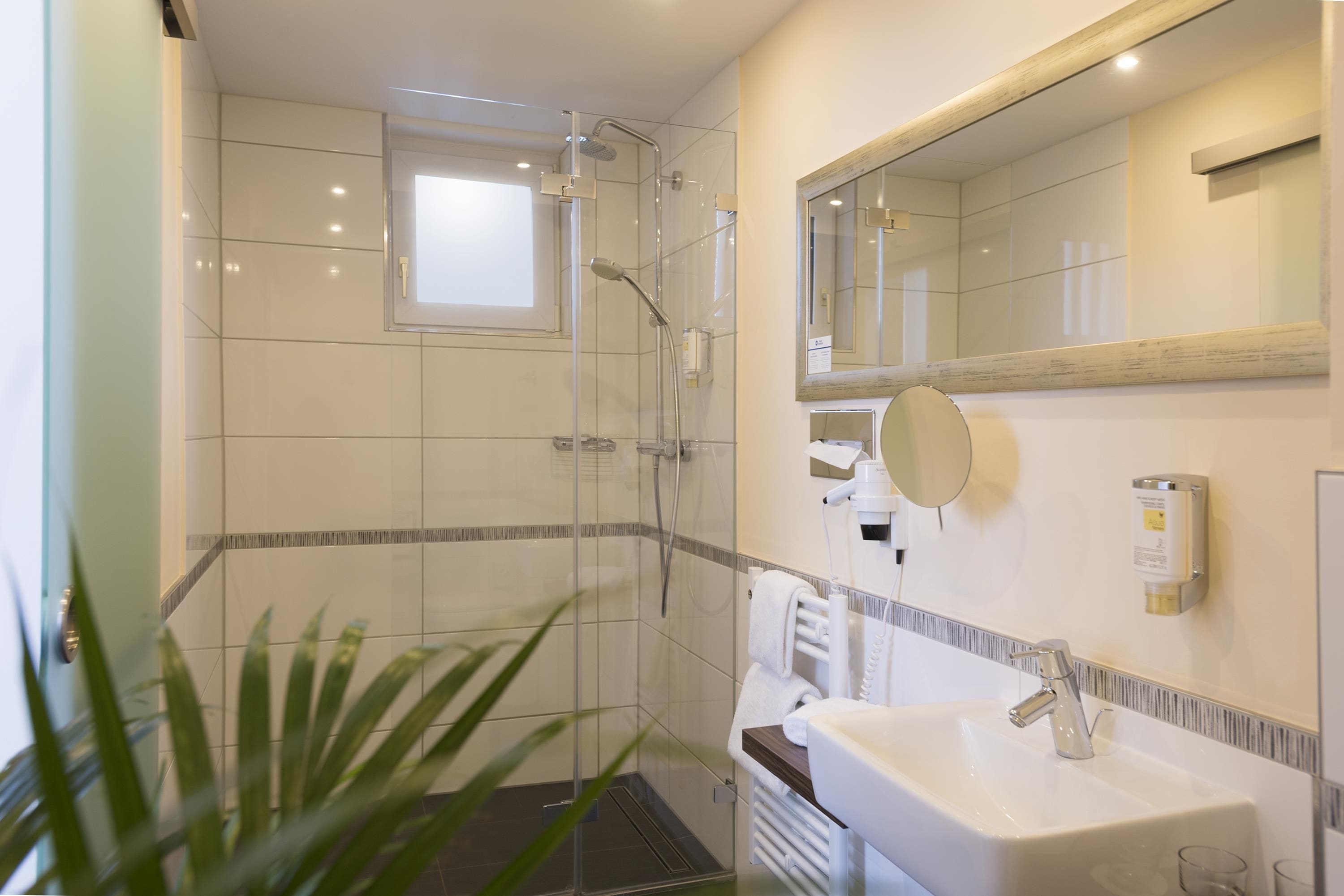 Un baño moderno con ducha envuelta en vidrio, un lavabo blanco y un espejo sobre el lavabo.