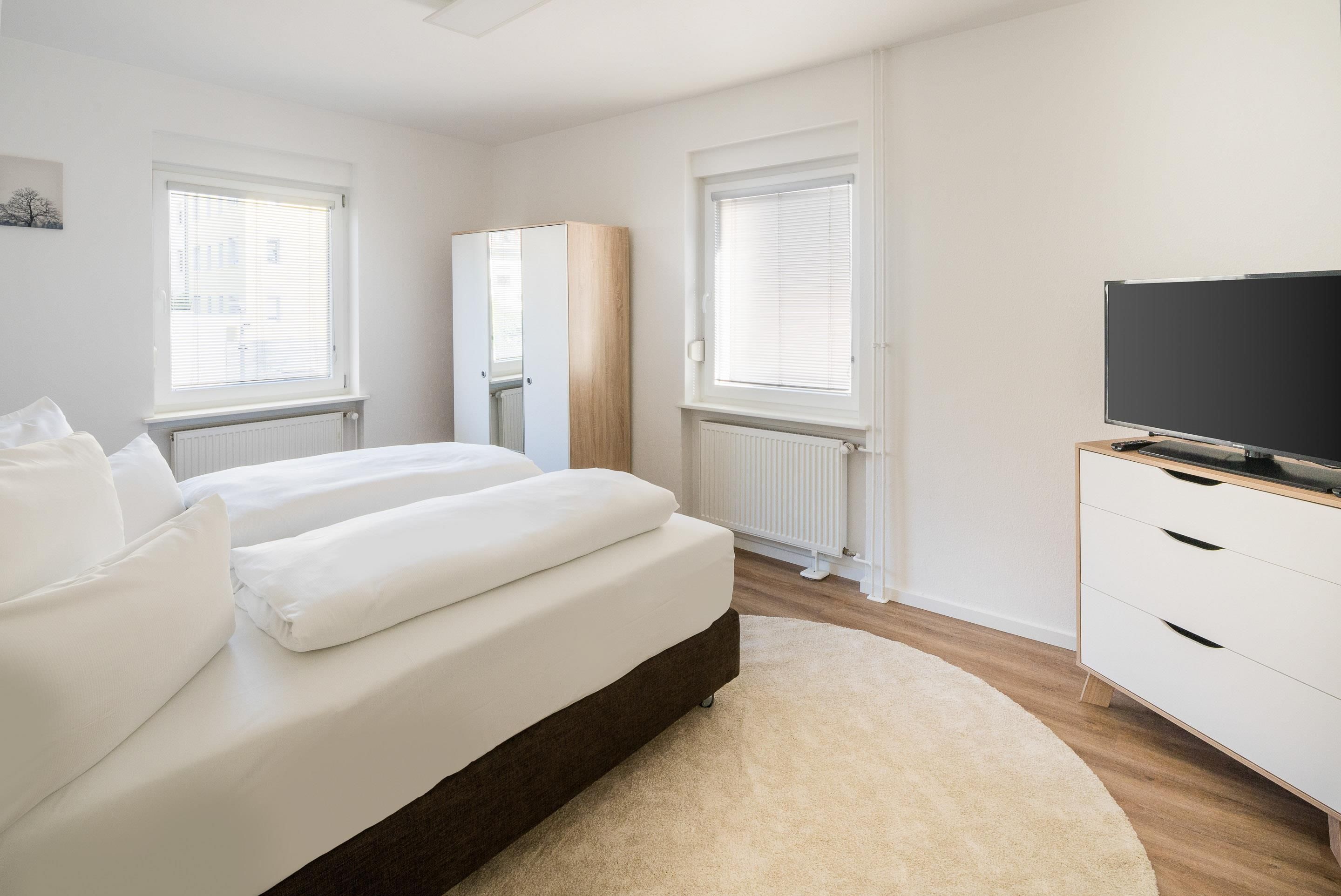 A modern bedroom with a bed, a TV, and a wardrobe.