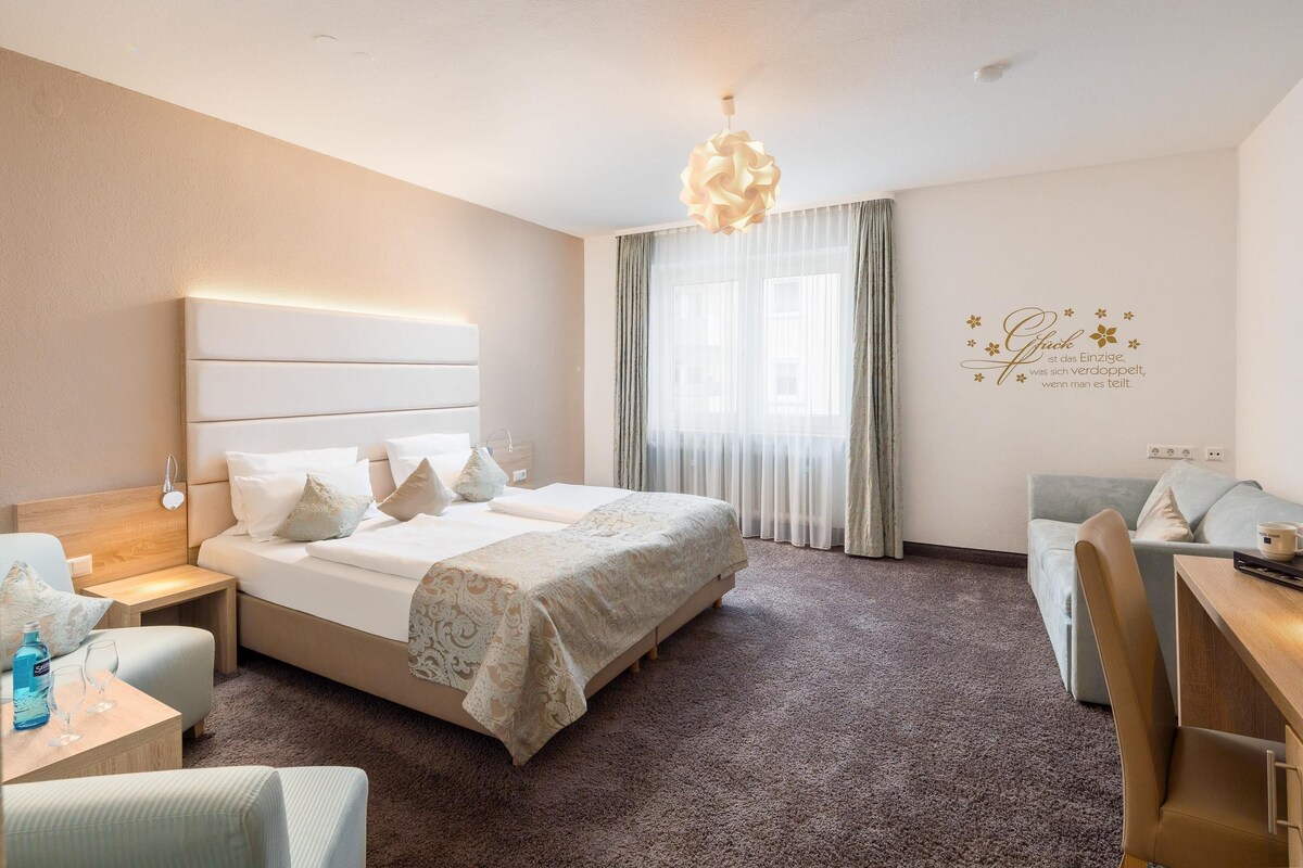 A hotel room with a large bed, a desk, a chair, and a sofa.