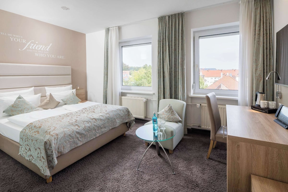 A hotel room with a bed, a glass table, a chair, and a desk.