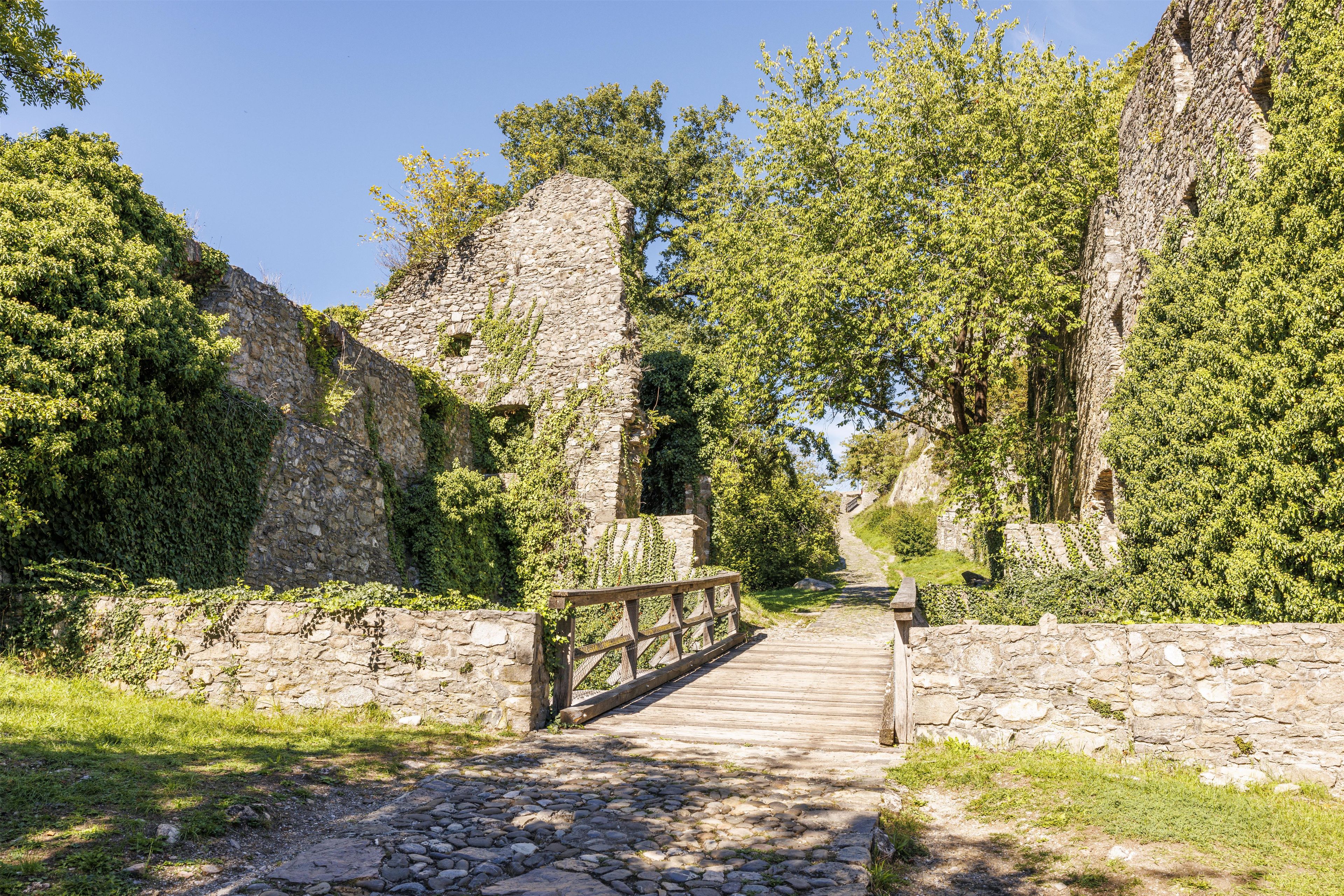 A stone pathway leading through ruins with a wooden bridge over a small stream.
