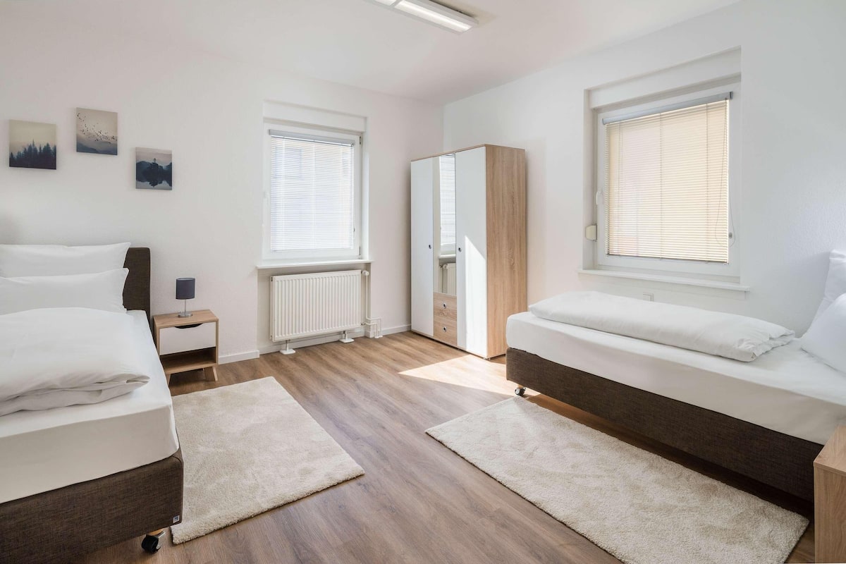 A modern bedroom with two beds, a wardrobe, and a radiator.