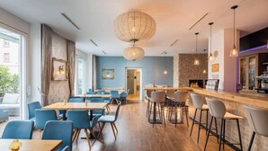 A modern restaurant with wooden tables and blue chairs, a bar area with stools, and a stone wall with a fireplace.