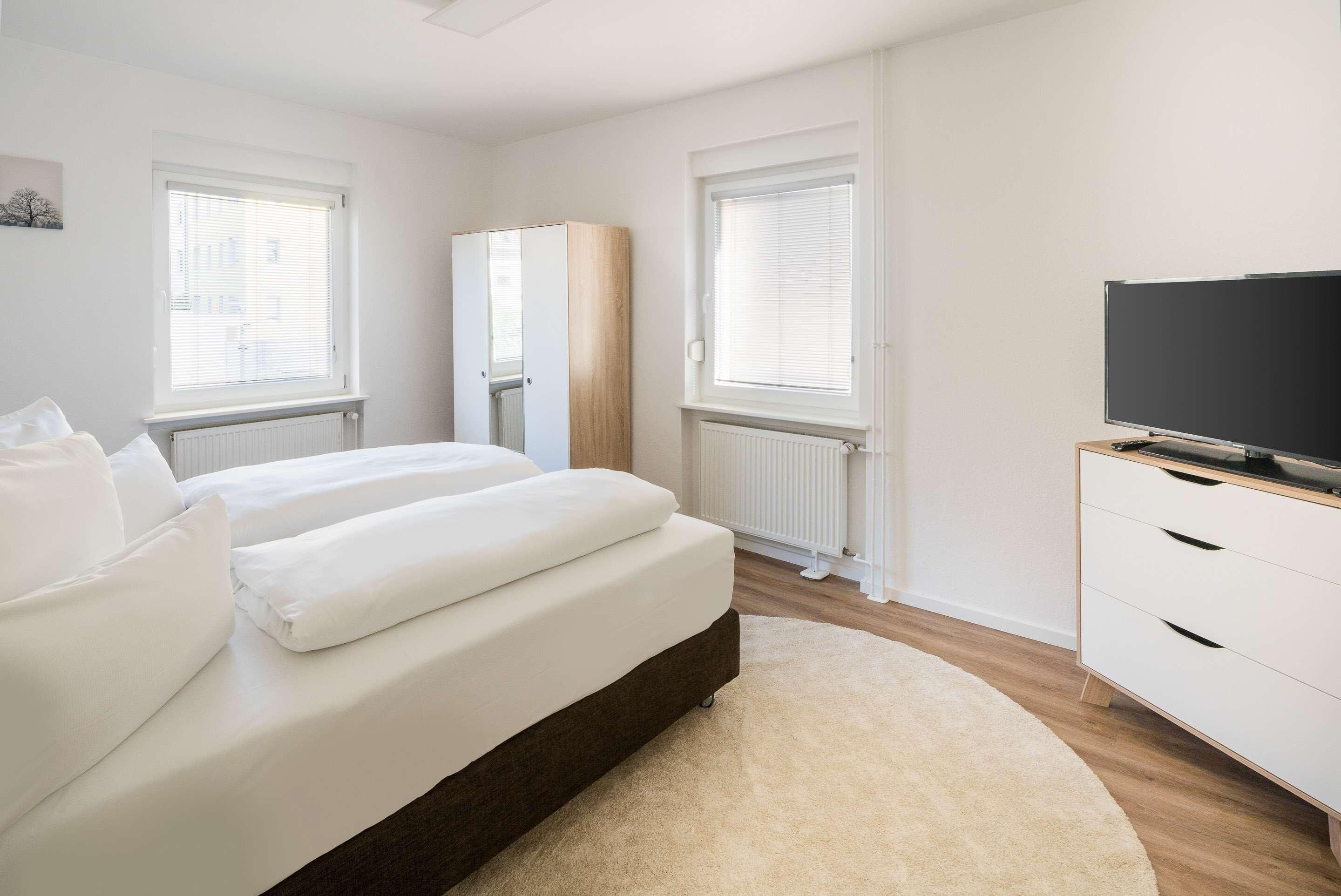 A modern bedroom with a bed, a wardrobe, a television, and a radiator.