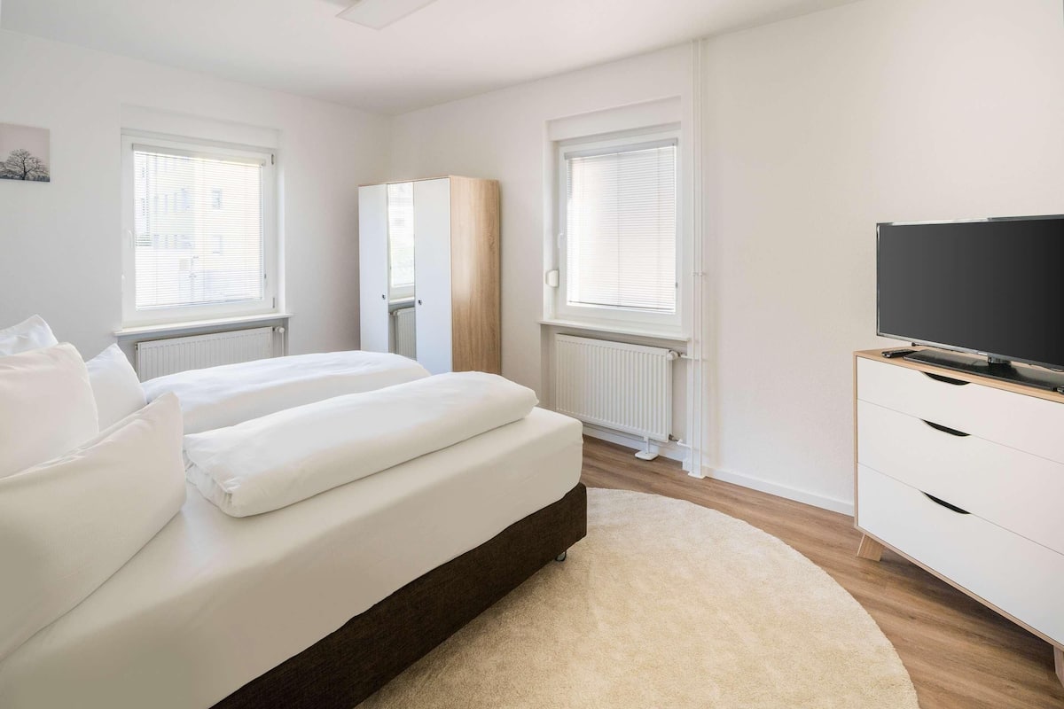 A modern bedroom with a bed, a wardrobe, a television, and a radiator.