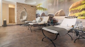 A spa area with a stone wall, a hanging chair, and two lounge chairs with towels.