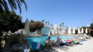 Relax by the pool surrounded by lush greenery and palm trees, with lounge chairs and umbrellas at your disposal.