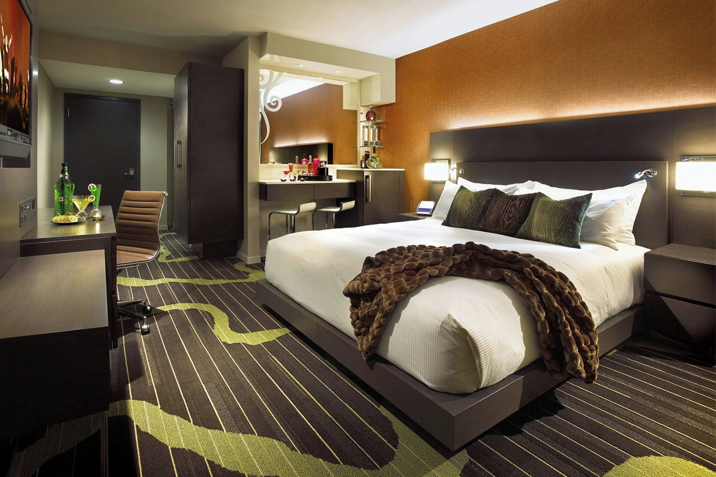 A hotel room with a large bed, a desk, a chair, and a minibar.