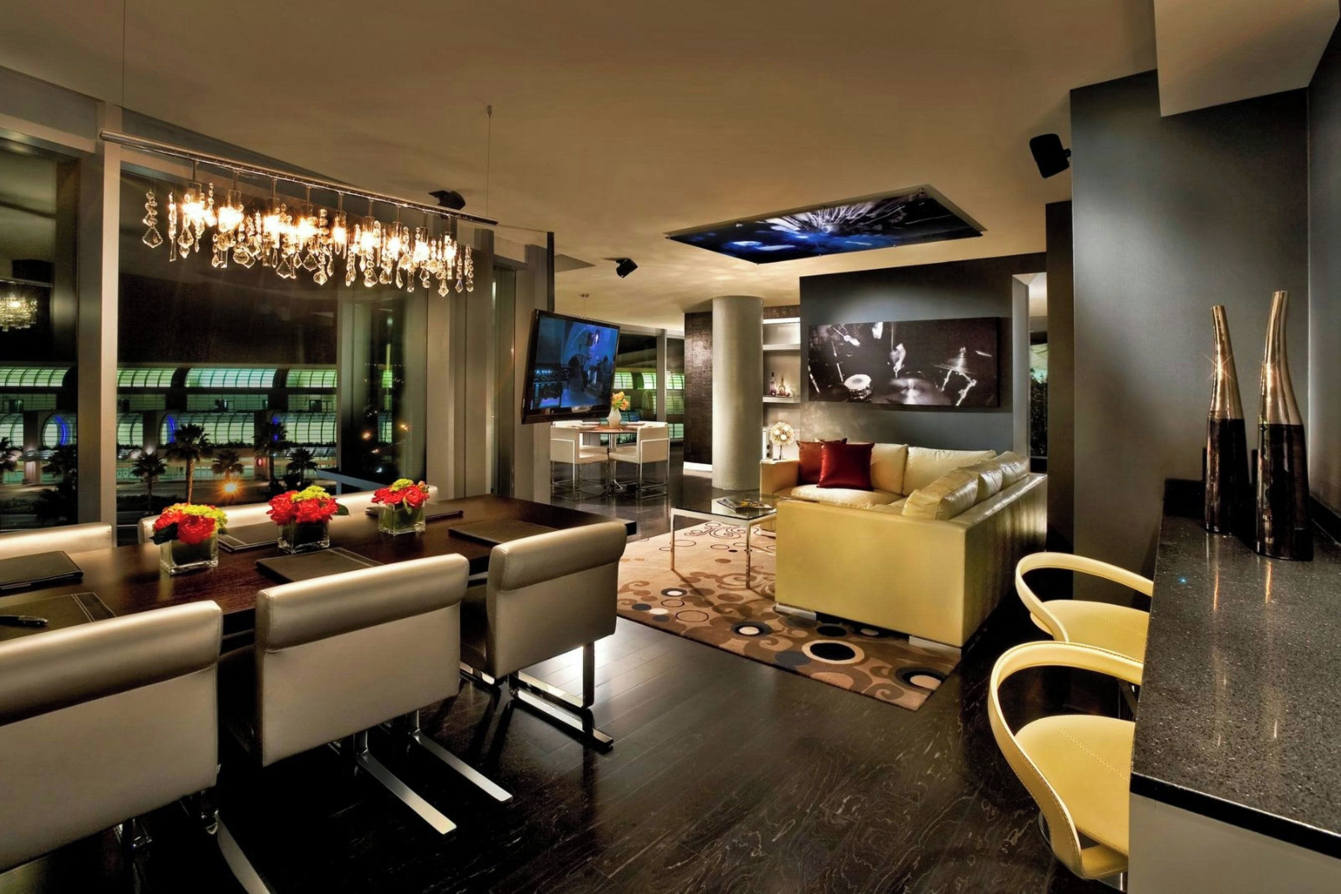 A modern living room with a dining area, a flat-screen TV, a bar area, and a large window with a view of the city.