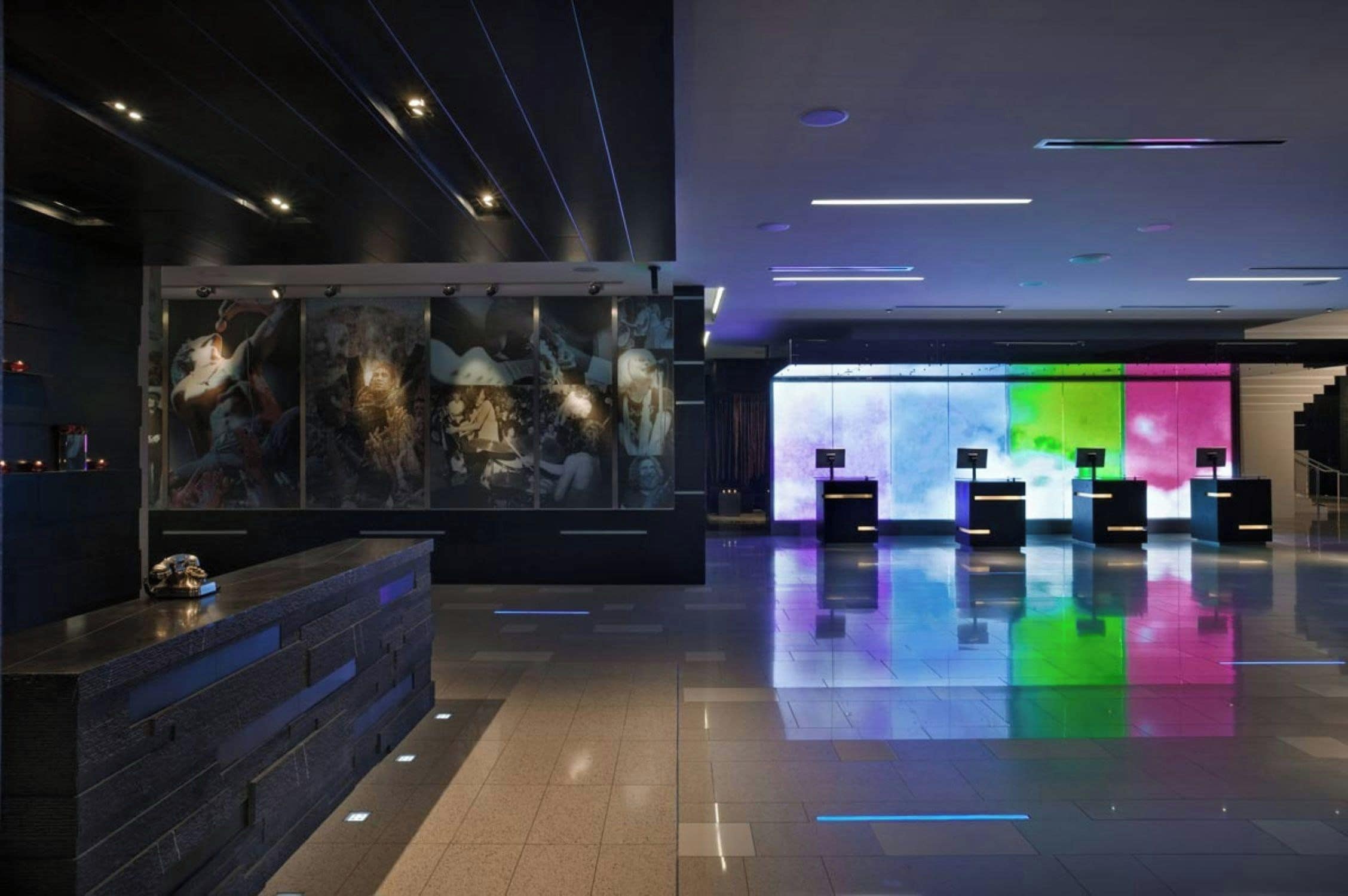 Un moderno vestíbulo de hotel con un mostrador de recepción, una obra de arte de gran formato y una pantalla digital colorida.