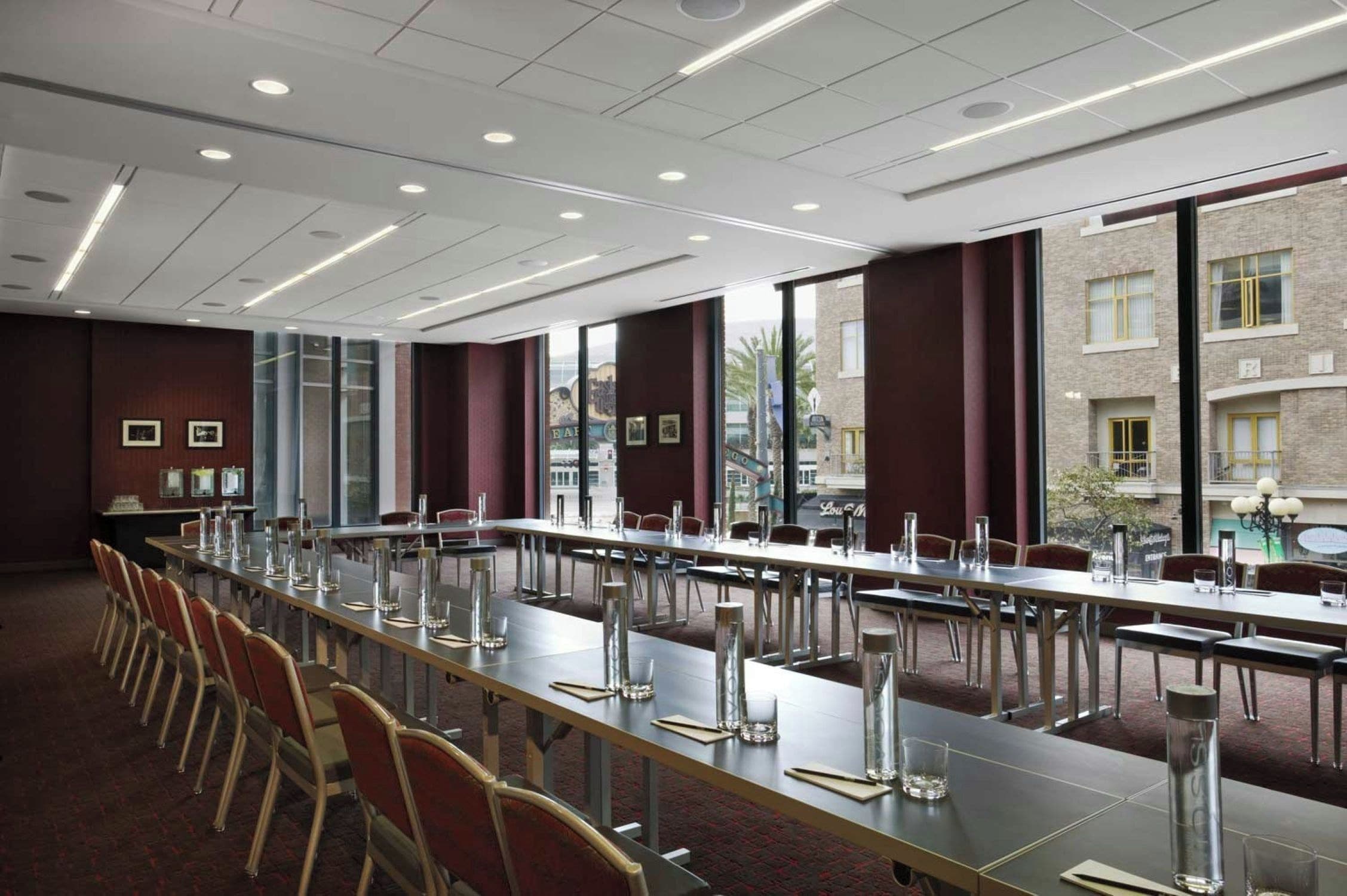 Un salón de conferencias con largas mesas, sillas y vistas a edificios a través de amplios ventanales.