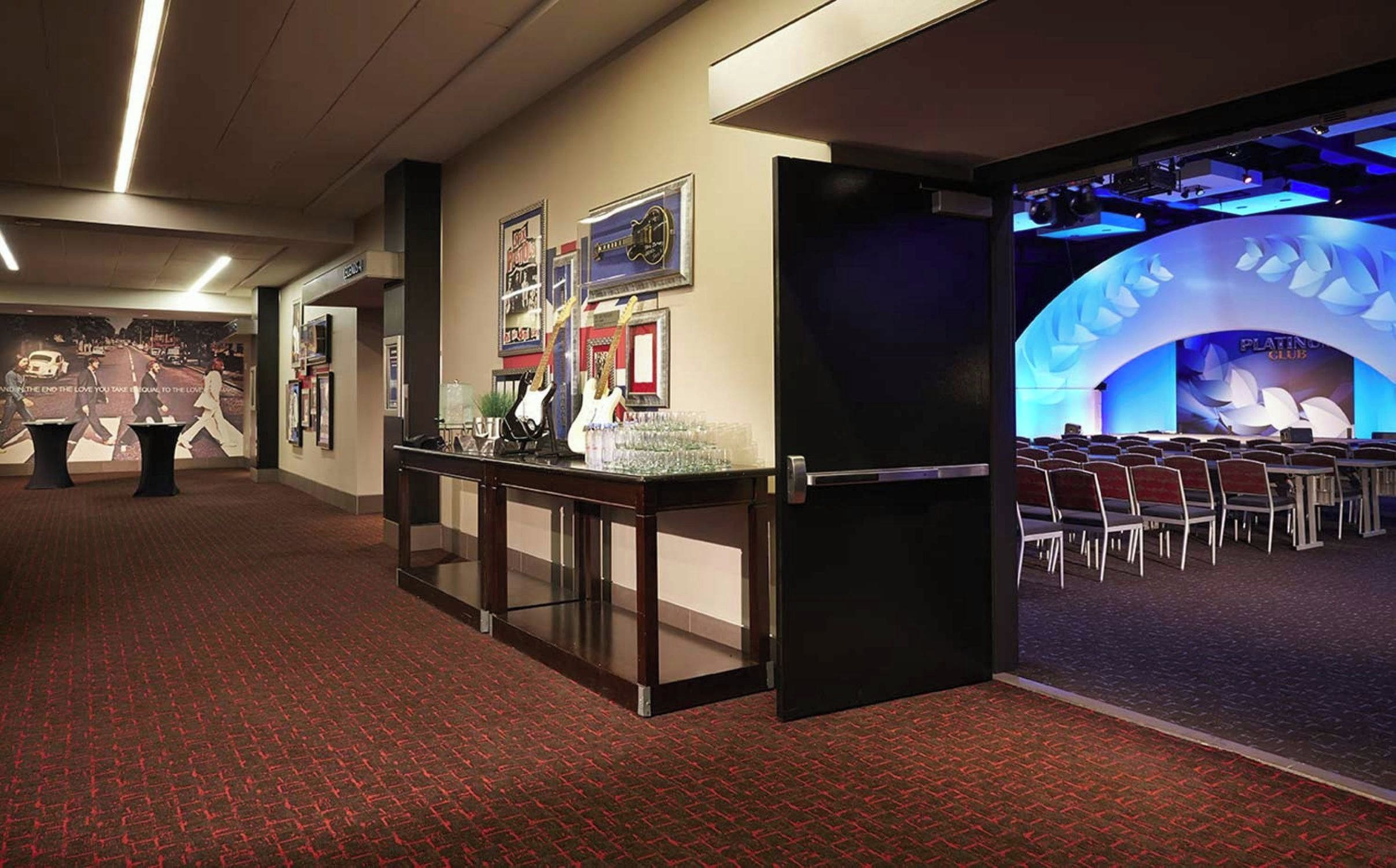 A hotel lobby with a reception desk, framed pictures on the wall, and a stage area with chairs.
