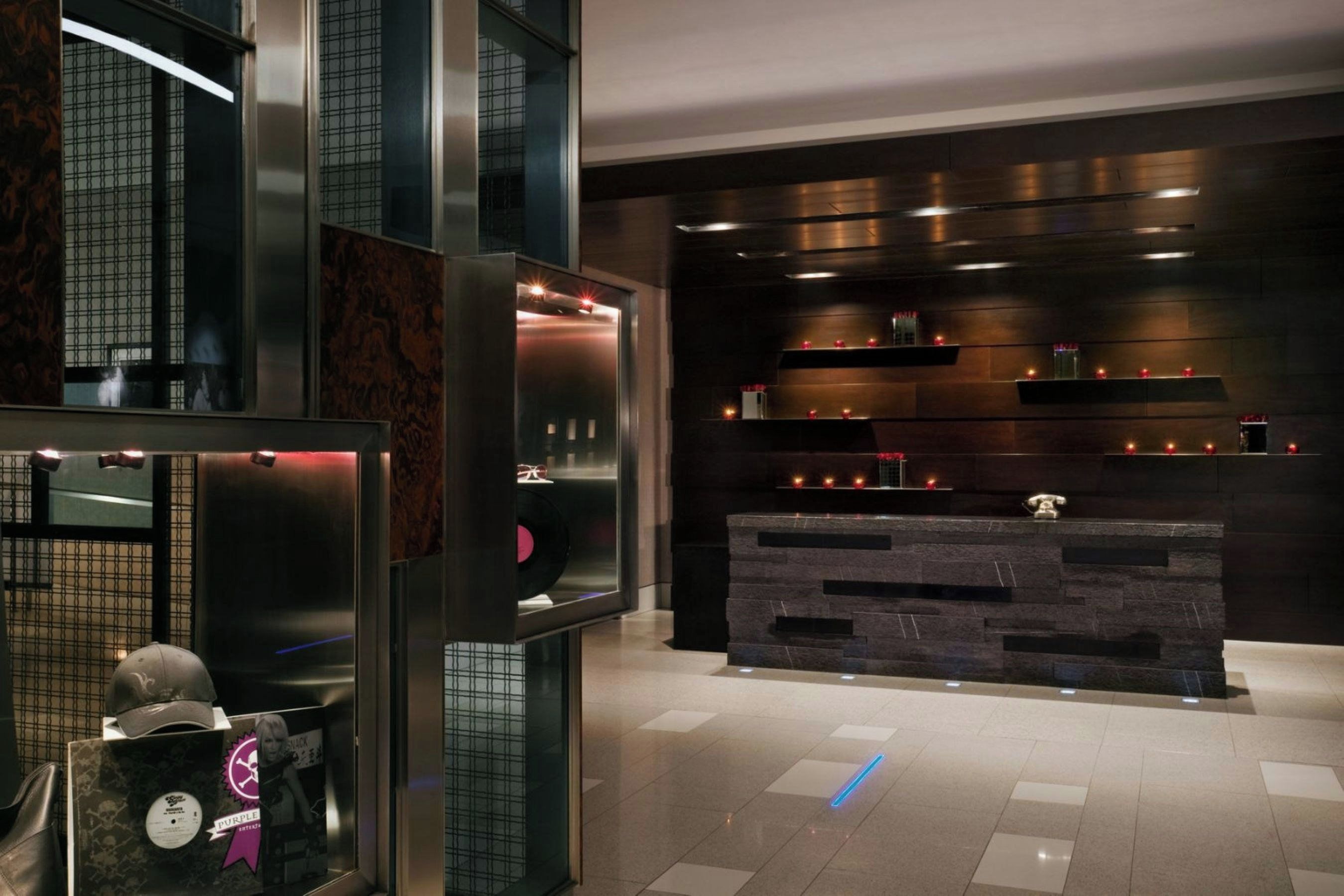 A modern lobby with a reception desk, a glass elevator, and a patterned wall.