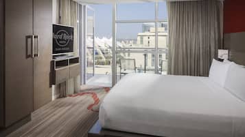 Ein Hotelzimmer mit einem großen Bett, einem Fernseher auf einem Schrank und Blick auf die Stadt durch große Fenster.