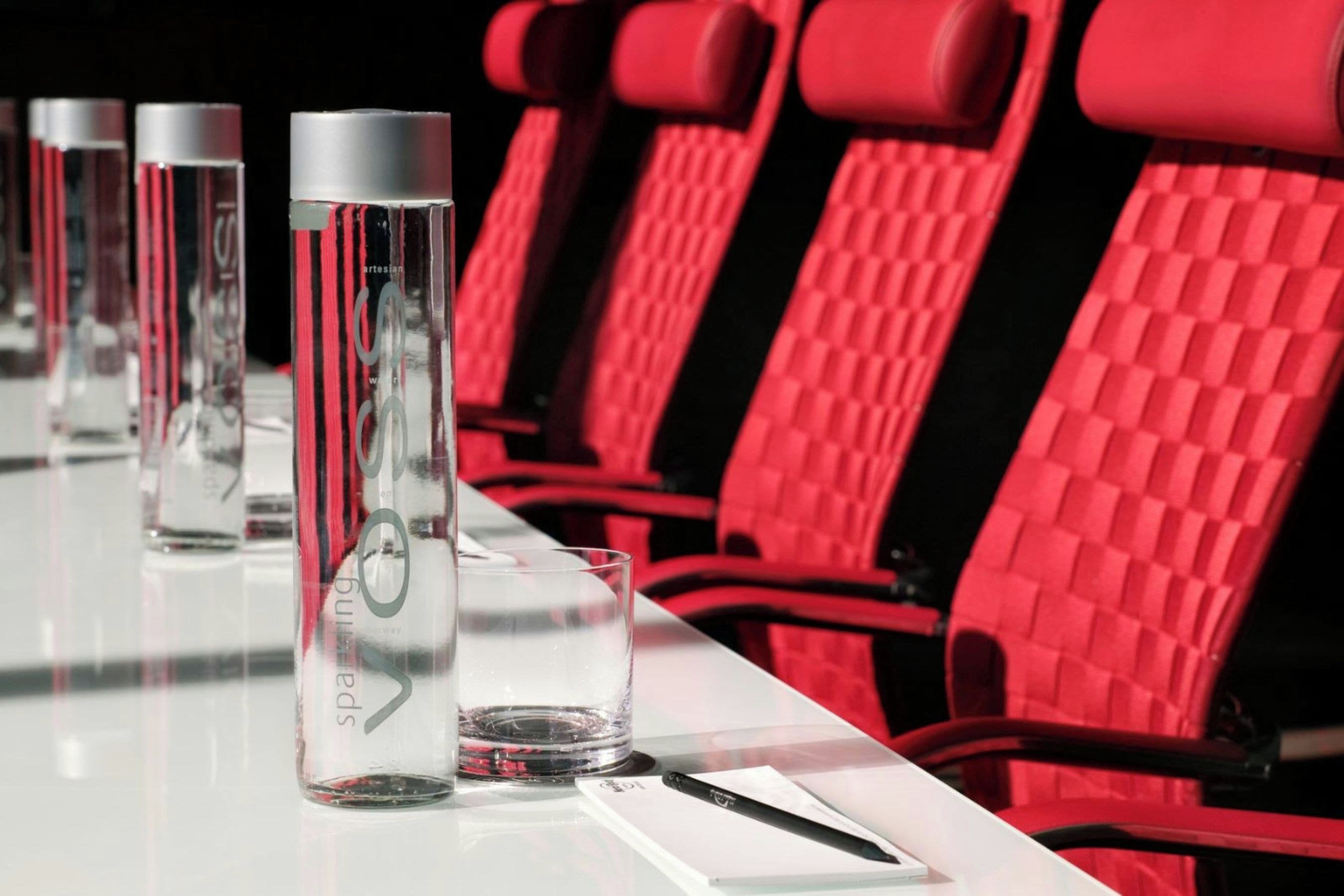 A row of red chairs with a textured backrest, a clear glass bottle, and a glass on a white table.