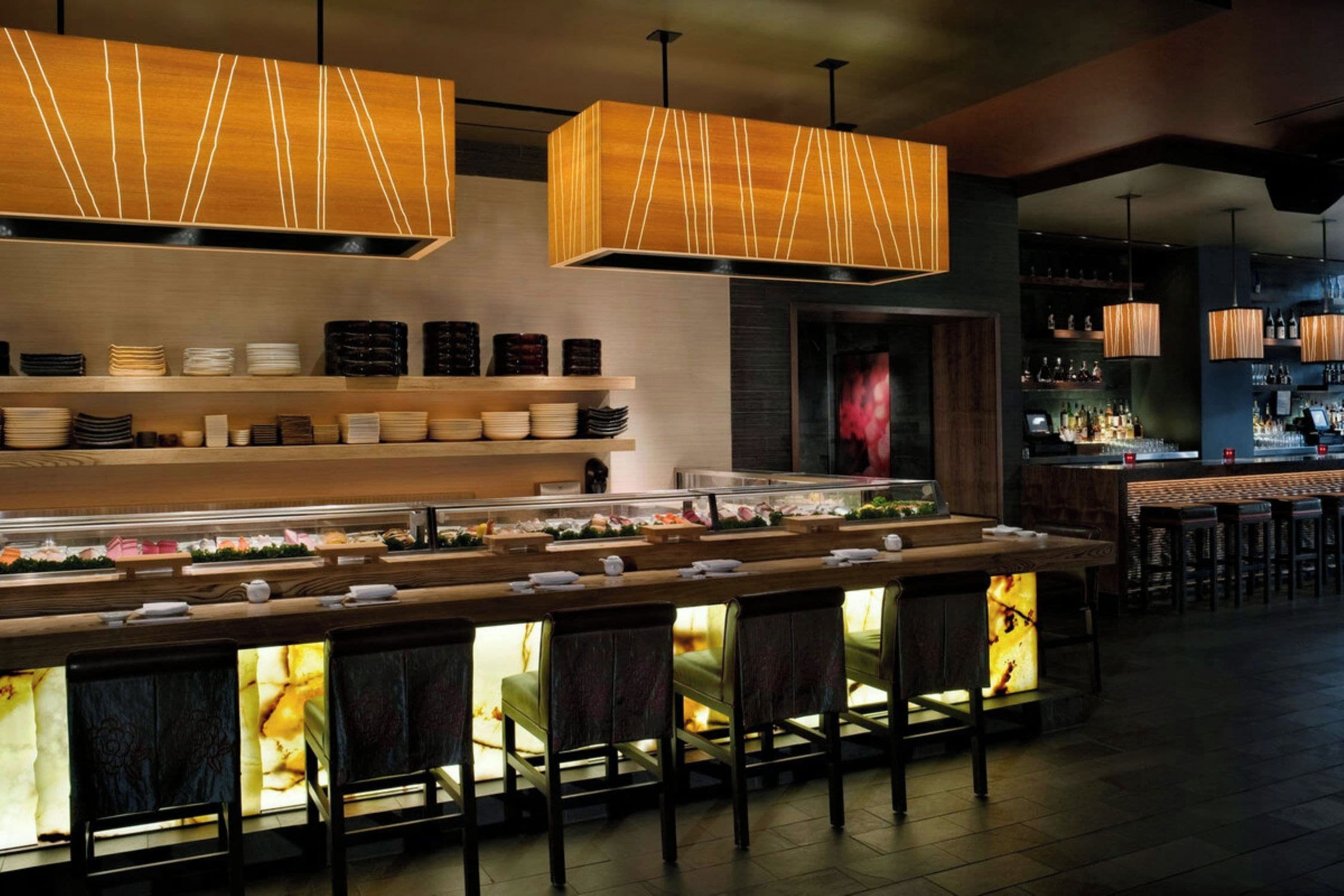 A bar area with a long counter, multiple seating options, and overhead lighting fixtures.