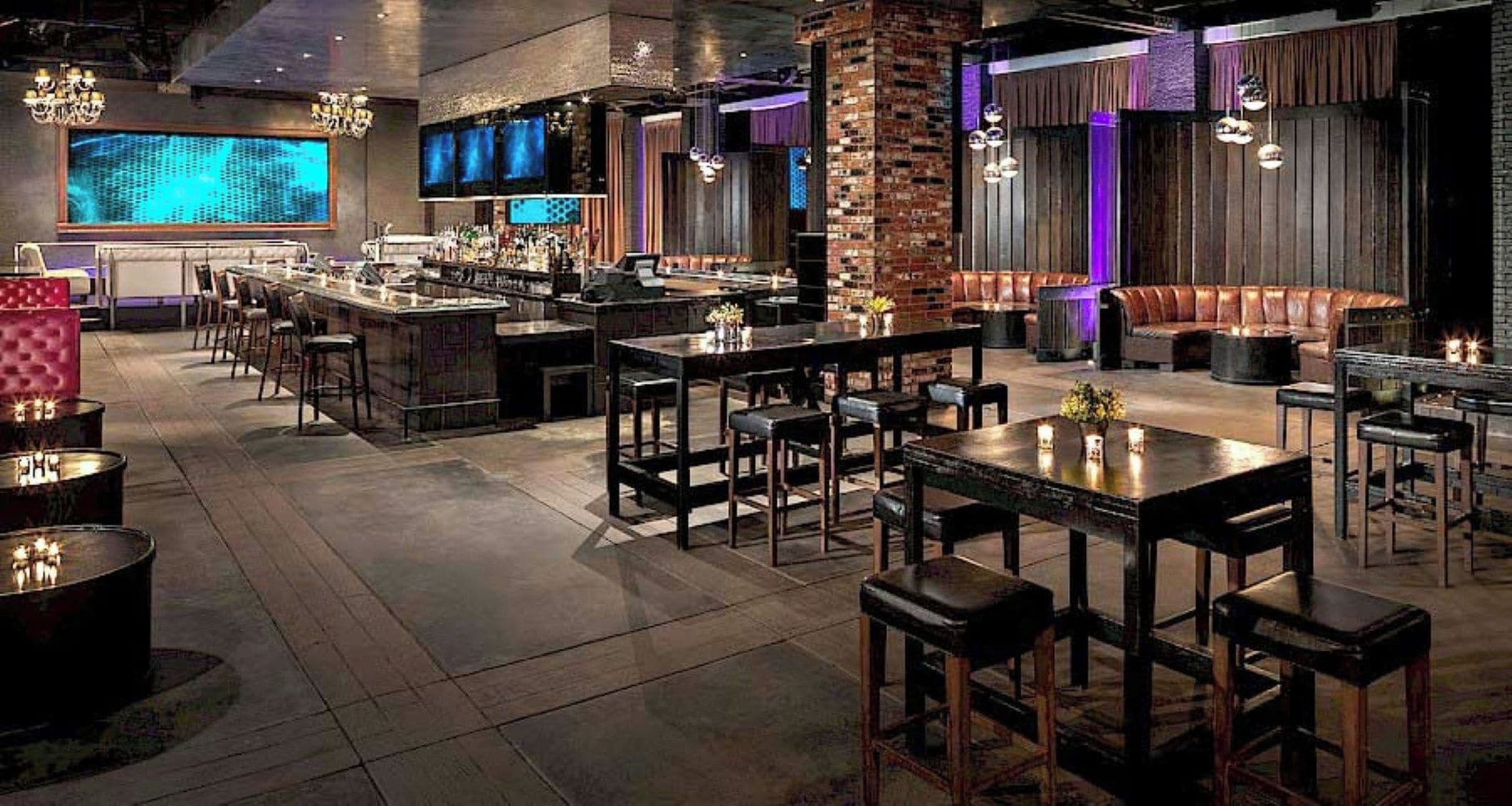 Un área de bar moderna con diversas opciones de asientos, incluidas mesas y cabinas, y una barra con una variedad de botellas.