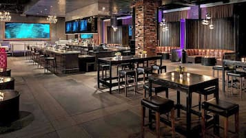 Un área de bar moderna con diversas opciones de asientos, incluidas mesas y cabinas, y una barra con una variedad de botellas.