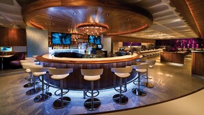 Zona de bar moderna con barra circular, varios taburetes y una pantalla grande.