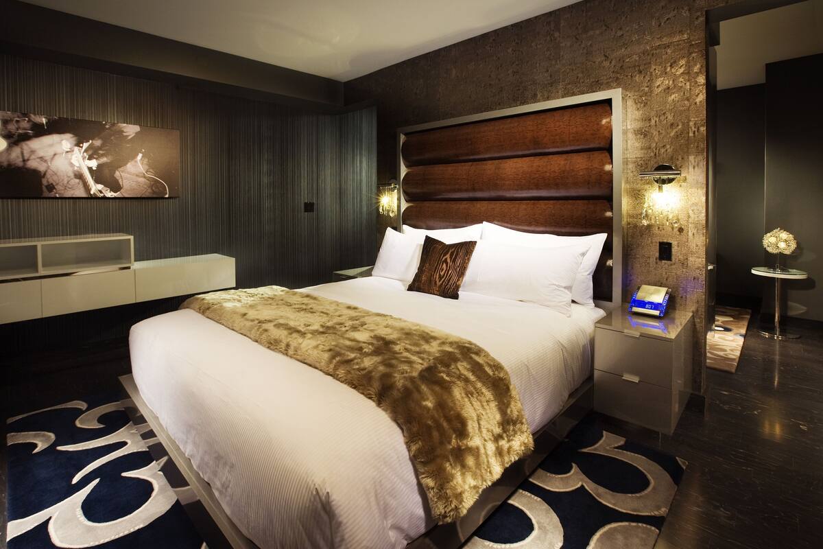 Una habitación de hotel moderna con una cama grande, un televisor de pantalla plana, una mesita de noche y un adorno en la pared.