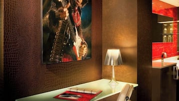 Habitación de hotel moderna con una mesa de vidrio, una silla blanca acolchada, una lámpara y una obra de arte enmarcada en la pared.