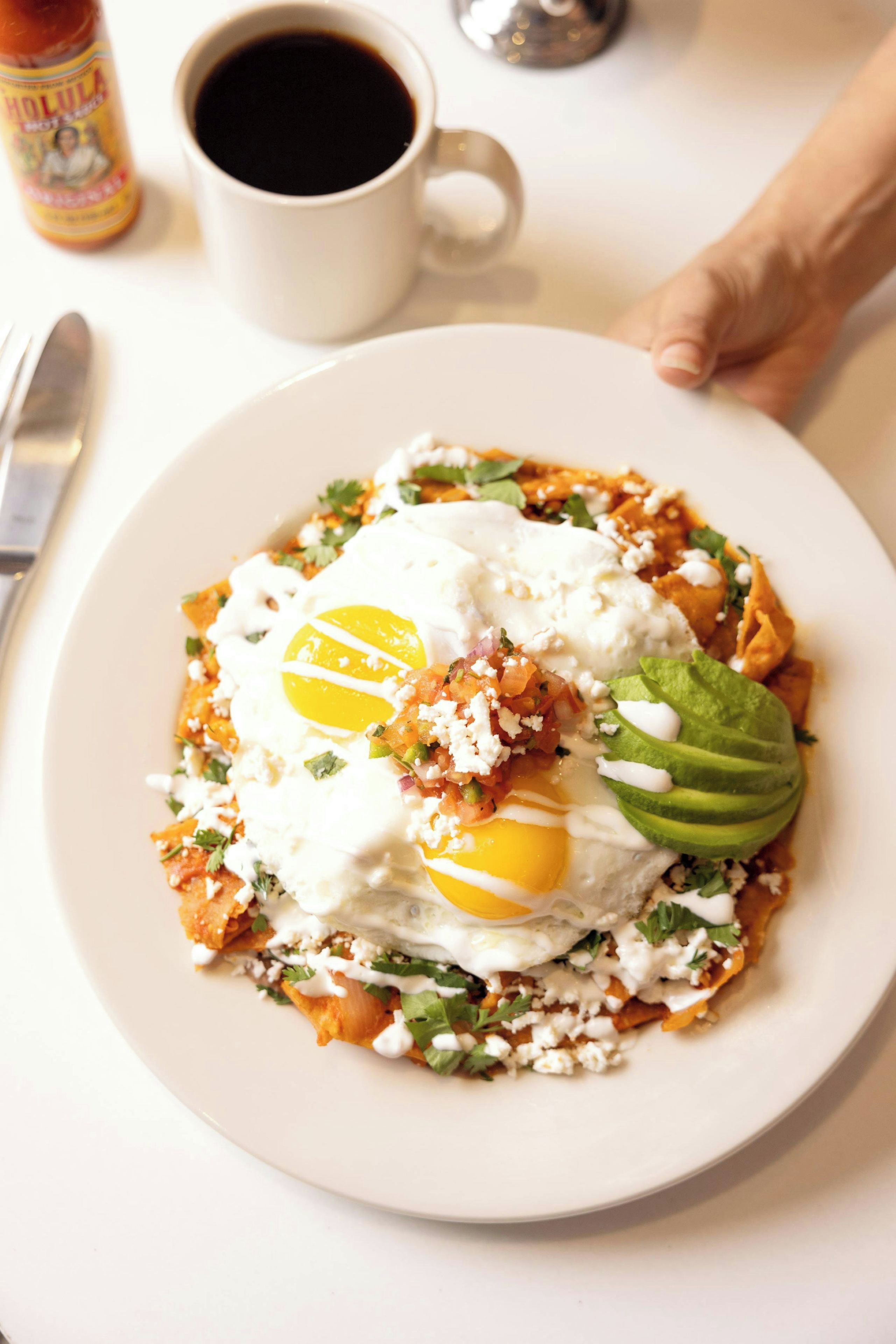 A plate of food with an egg, avocado, and cheese on a white plate.