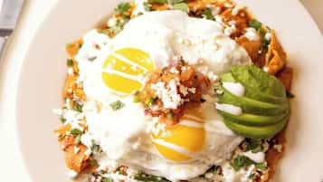 A plate of food with an egg, avocado, and cheese on a white plate.