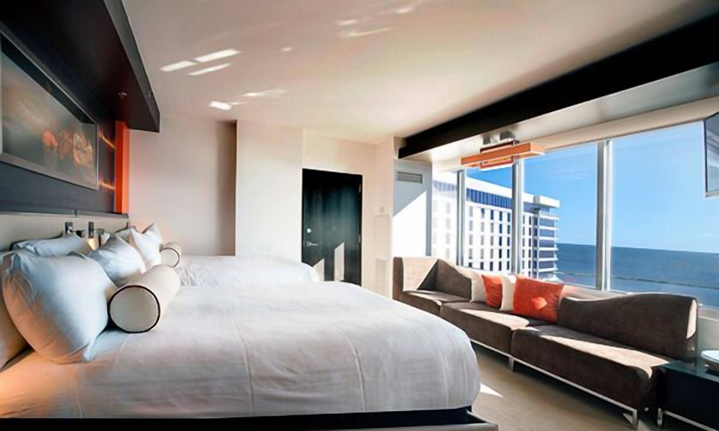 A modern hotel room with a large bed, a sofa, and a view of the ocean.