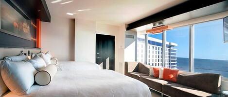 A modern hotel room with a large bed, a sofa, and a view of the ocean.