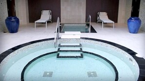 Piscina com fundo de vidro, rodeada por espreguiçadeiras e grandes vasos.
