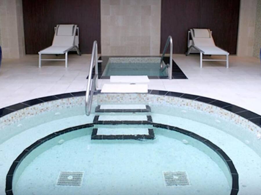 A swimming pool with a glass bottom, surrounded by lounge chairs and large vases.