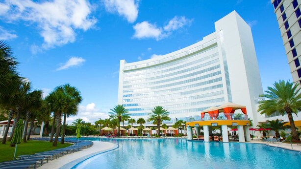 Um hotel grande com piscina, palmeiras e céu azul límpido.