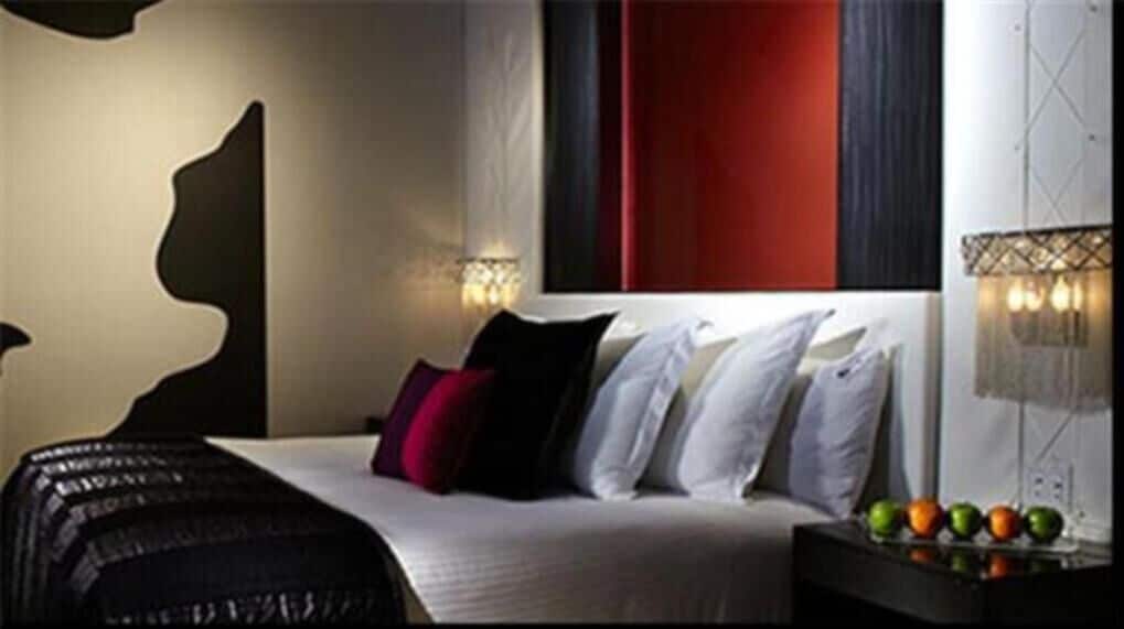 Quarto de hotel moderno com uma cama grande, uma obra de arte na parede e uma cesta de frutas no criado-mudo.