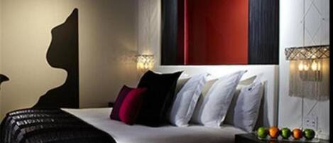 Quarto de hotel moderno com uma cama grande, uma obra de arte na parede e uma cesta de frutas no criado-mudo.