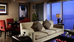 Quarto de hotel com sofá, duas poltronas, mesa de centro e vista para o oceano através de grandes janelas.