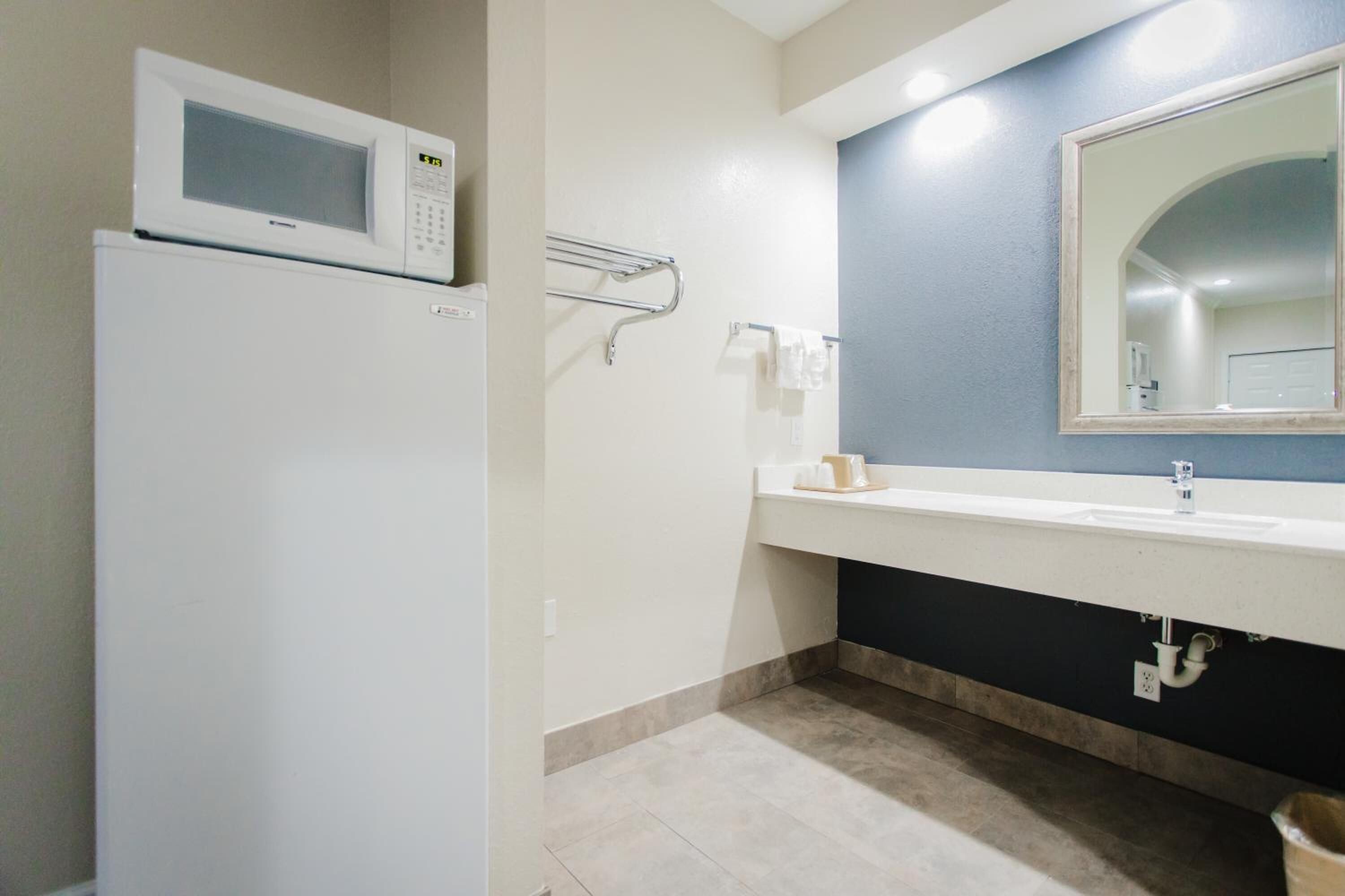 A bathroom with a white refrigerator, a sink with a mirror, and a towel rack.